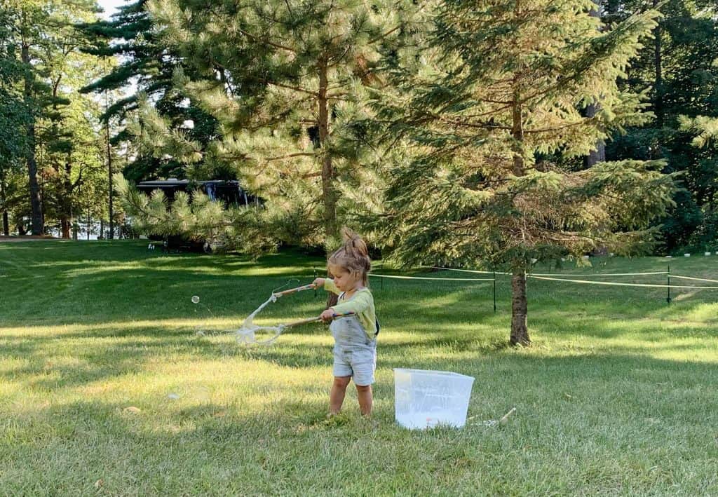child playing with DIY bubble wand making giant bubbles in field