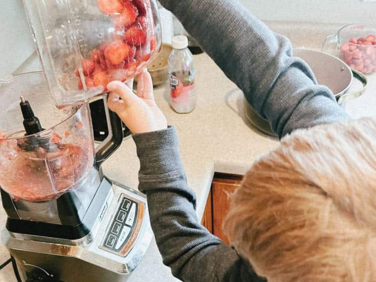 child pouring in strawberries into food processor to puree.