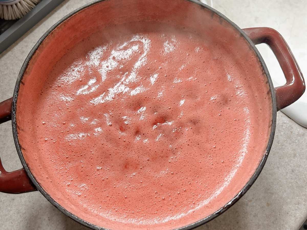 pot of strawberries that has been boiled and there is foam at the top to scrape off.