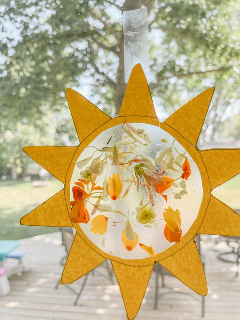 yellow construction paper sunshine craft with pressed flower suncatcher on window
