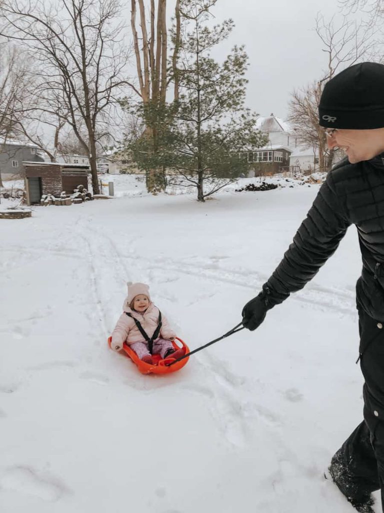 child being pulled on sled by her father in winter