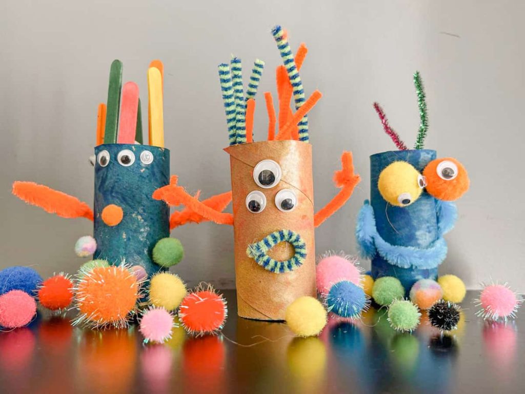 3 completed toilet paper roll monsters with pom poms around them