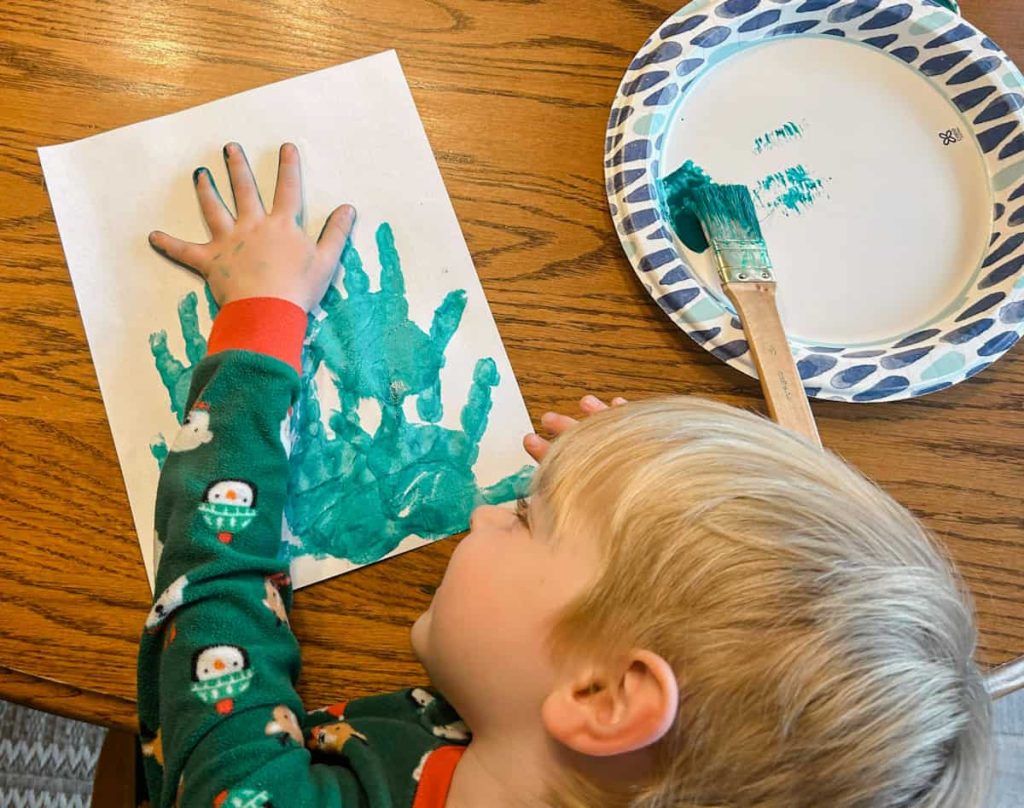 Toddler sticking painted hand on paper to create top of the Christmas tree