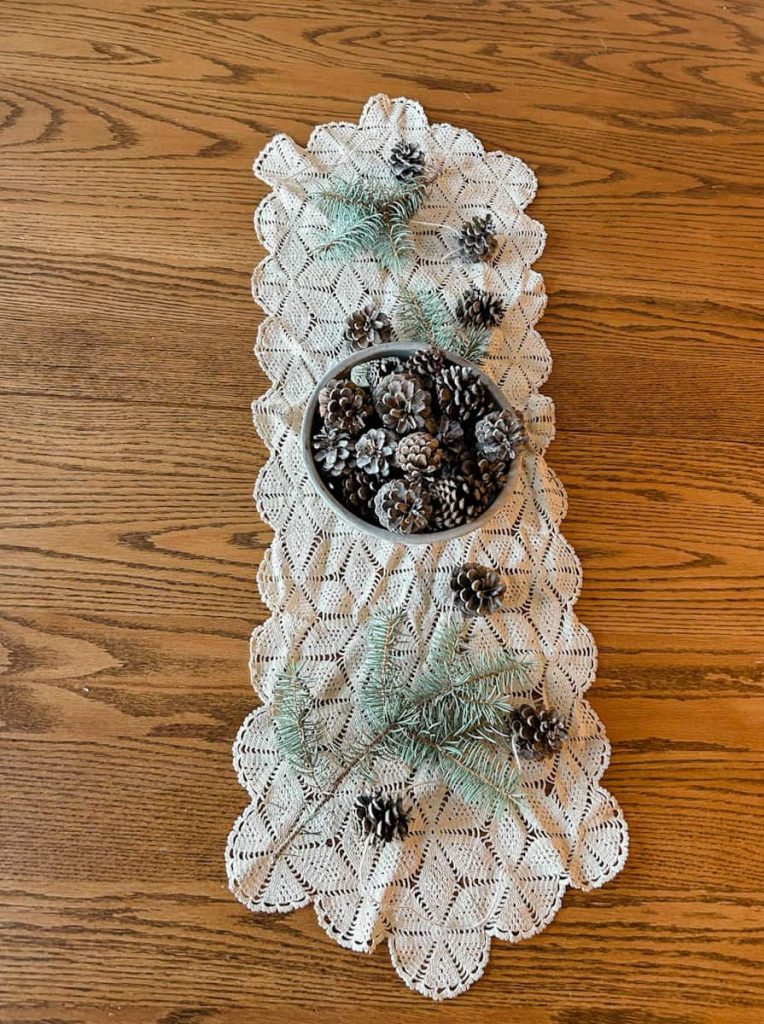 pinecone garland on top of table runner with greenery around it