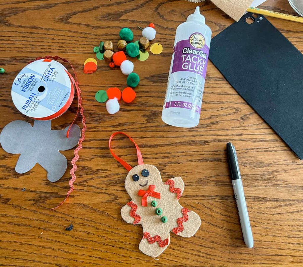 supplies for felt gingerbread man on table- supplies include sharpie, ribbon, pom poms, gingerbread man cut out and tacky glue