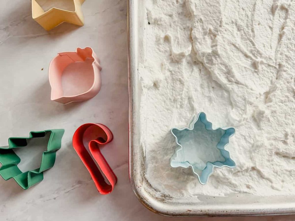 cookie cutters next to a baking pan with a sheet of homemade whip cream layered on it