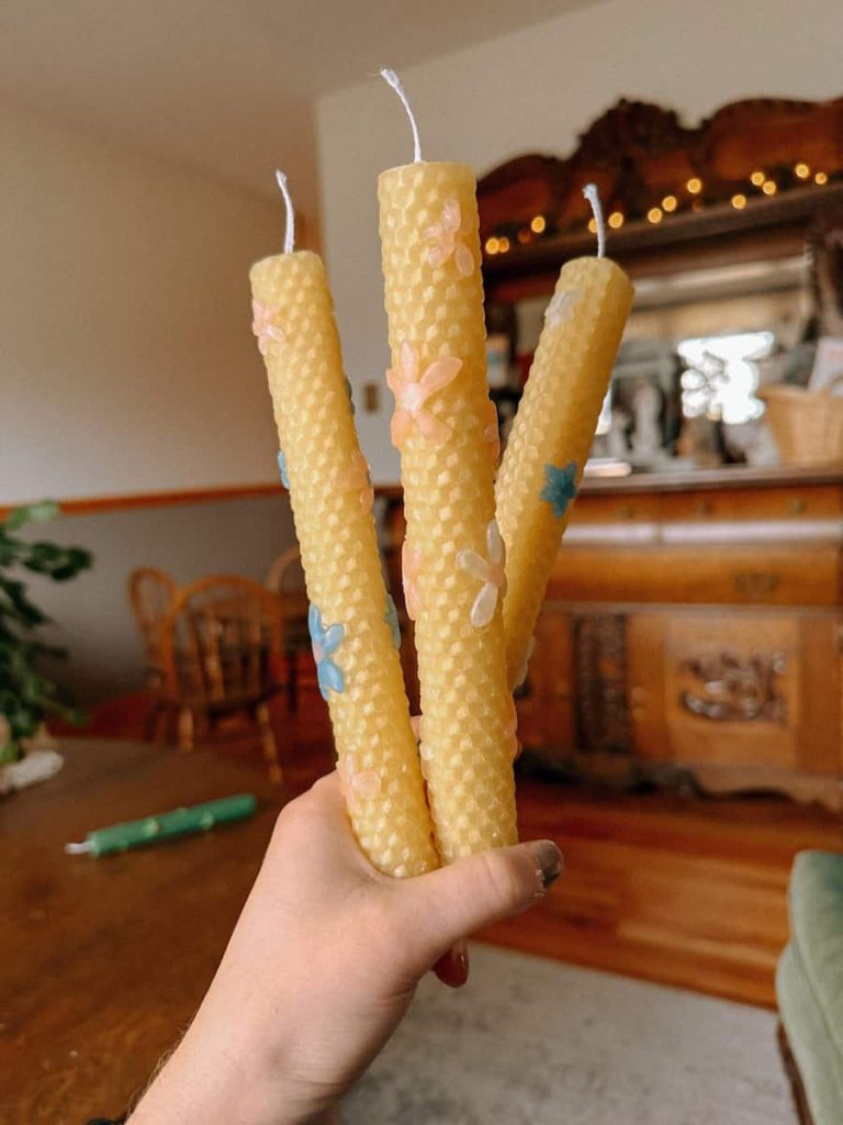 three hand rolled beeswax candles with flower designs held up in front of a dresser