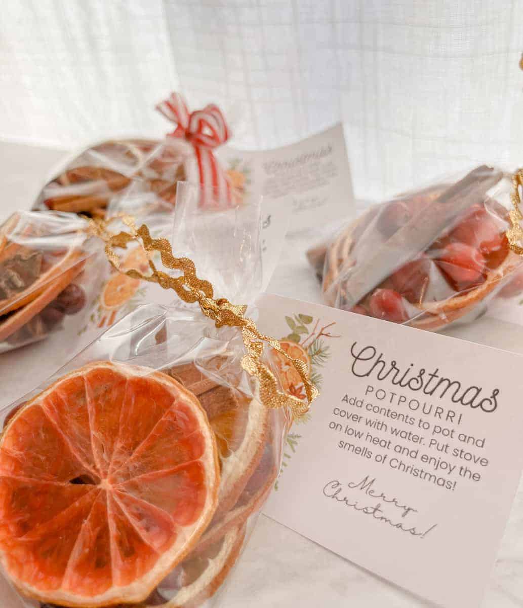 A set of gift bags with gold ribbon and dried potpourri ingredients wrapped with a gift tag for Christmas potpourri sitting on the counter.