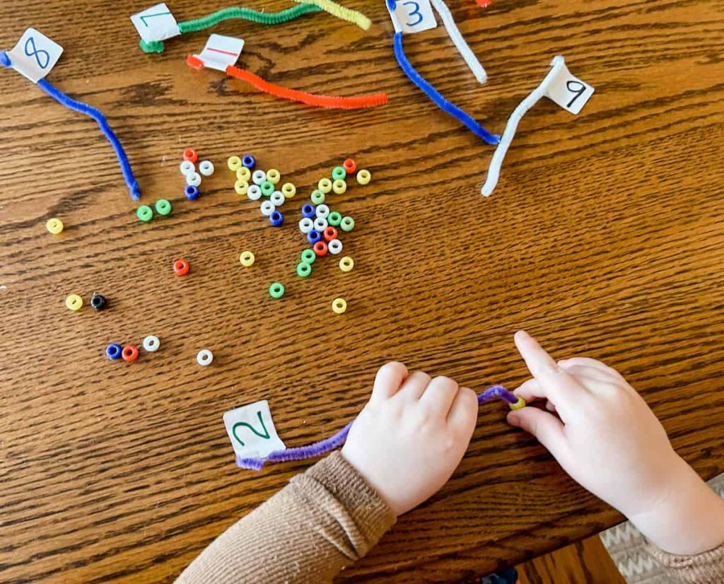child's hand stringing bead on pipe cleaner