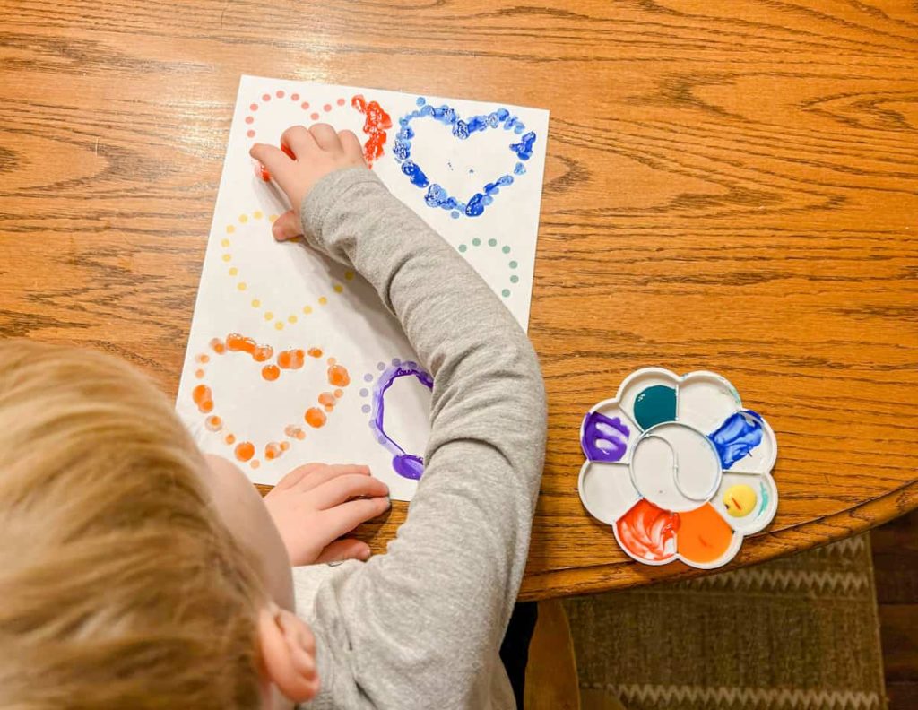 Child tracing red heart on printable with paint