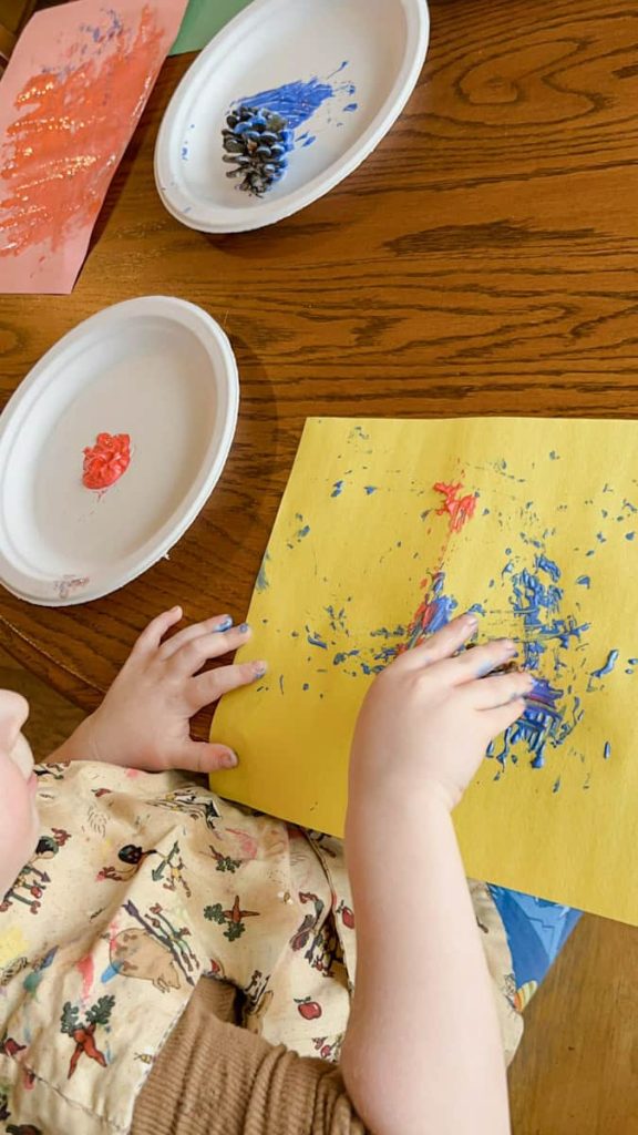 child sitting at table painting with pine cone