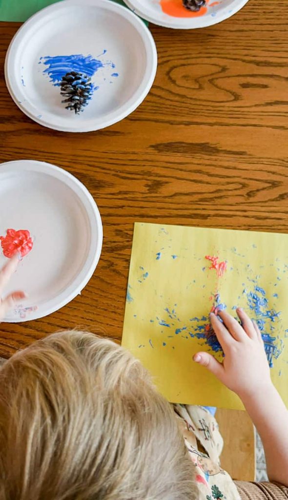 child sitting at table painting with pine cone