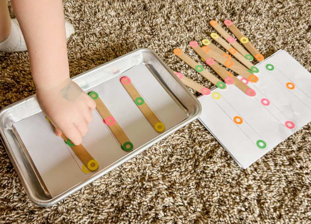 child's hand placing stick on pattern card playing the popsicle stick color matching activity