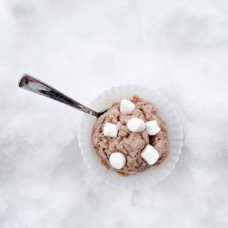 A bowl of chocolate snow ice cream with marshmallows on top in the snow