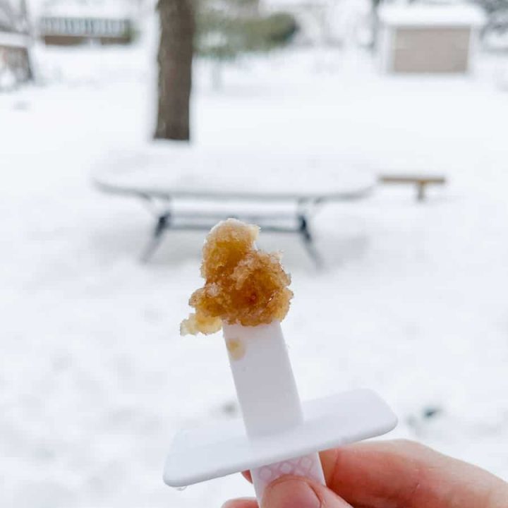 maple syrup taffy on a popsicle stick held up in front of snow