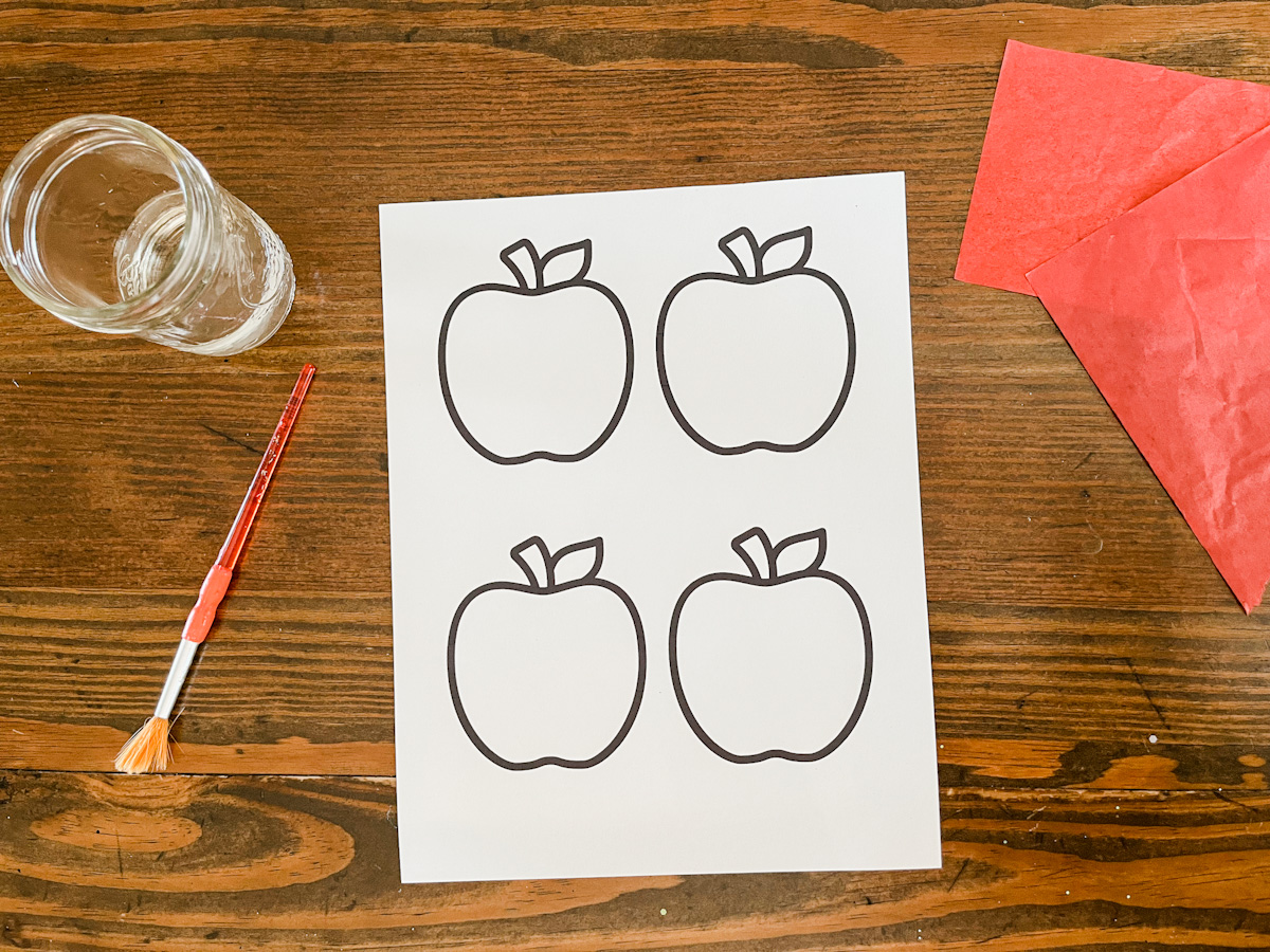 free apple template next to a paint brush and water and red tissue paper.