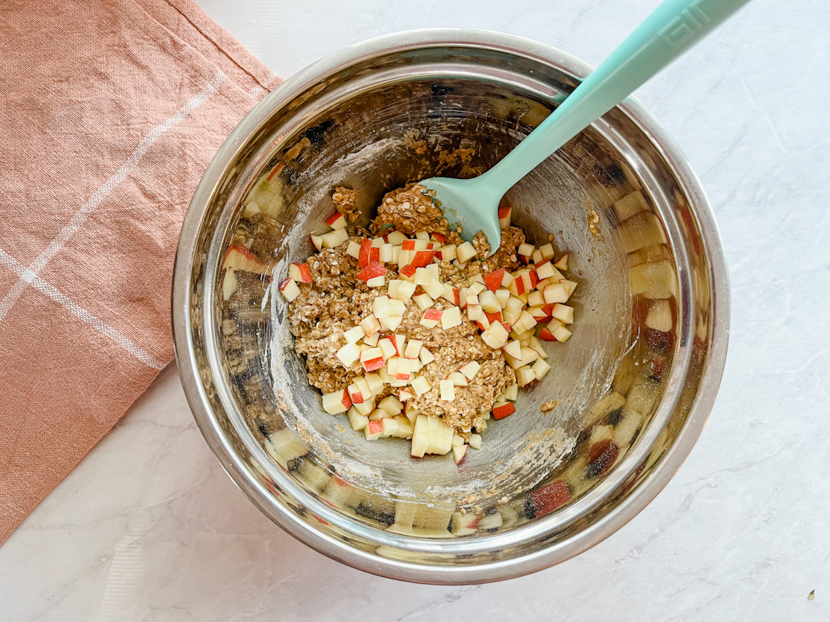Bowl of apple cinnamon oatmeal cookie dough with apples being folded in.