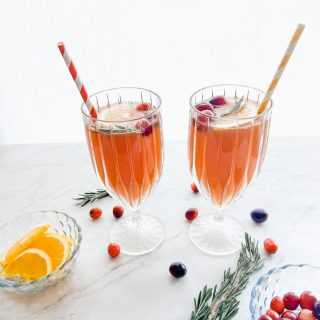 2 cups of holiday christmas punch next to each other surrounded by the punch garnish