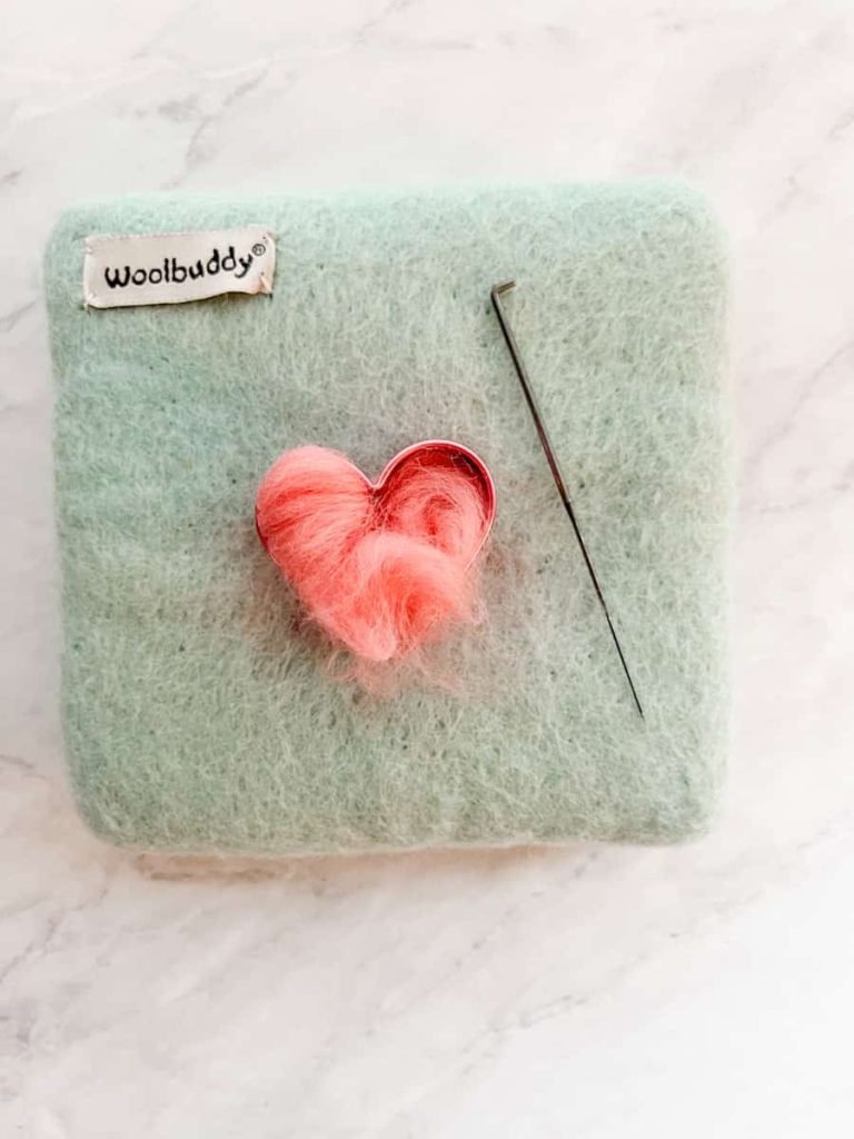 wool roving layered inside the heart cookie cutter on the felting mat