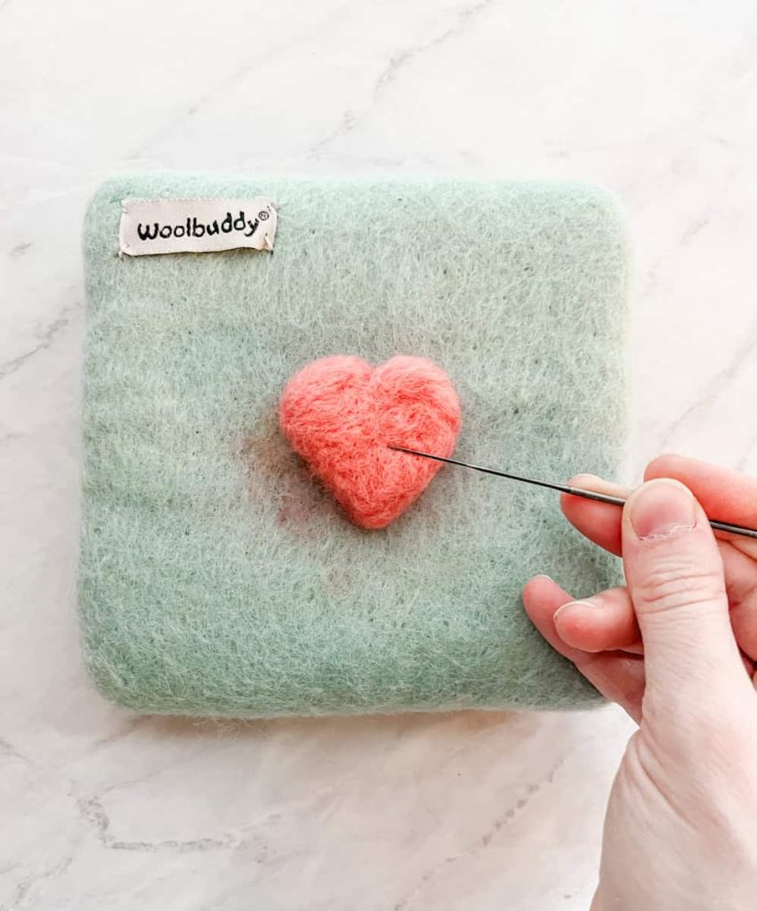 smoothing out the felt heart by poking gently at an angle on top of the felted heart on the felting pad