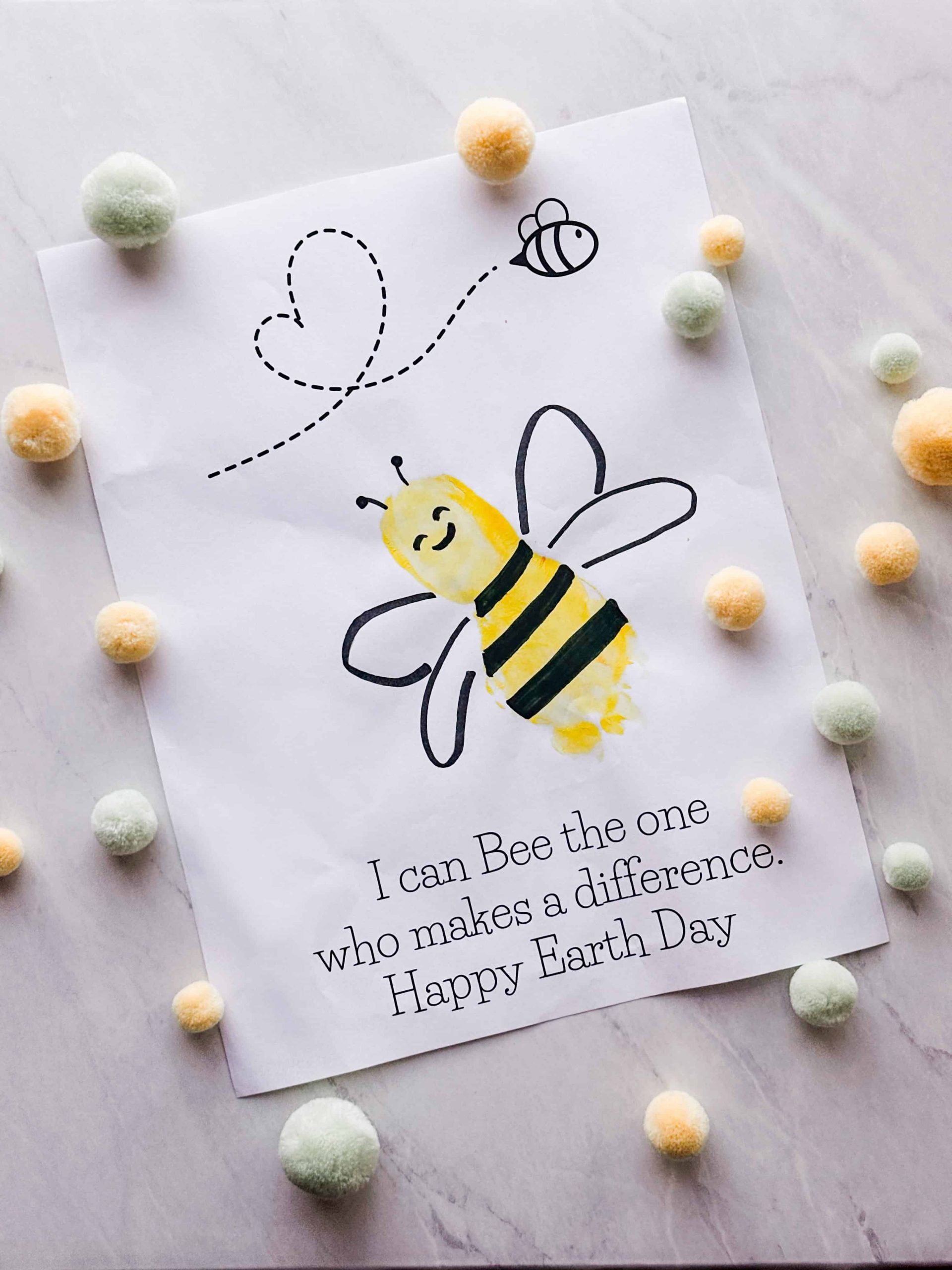 completed bee footprint craft on printable template with felt balls around the craft on a table
