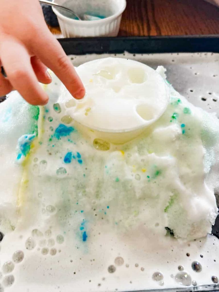 snow volcano erupting and child trying to pop the bubbles in the foam