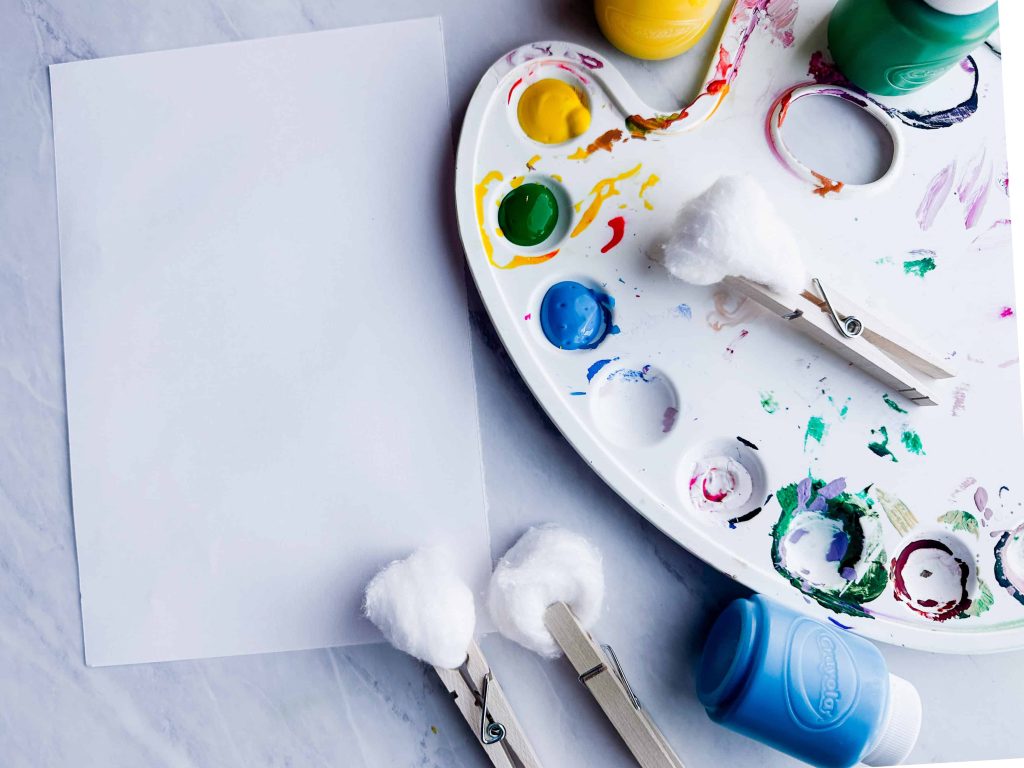 cotton balls next to art palate with paint and paper on table