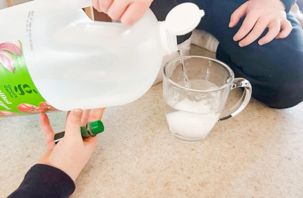 child pouring vinegar into the cup with the egg in it