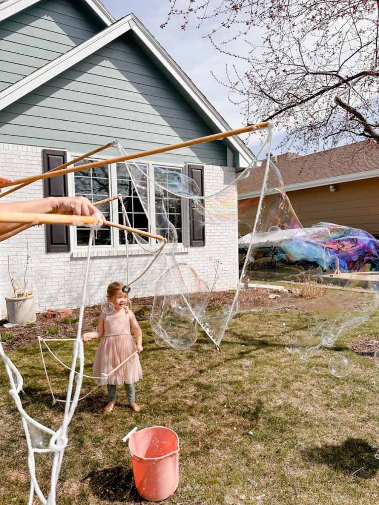 hand holding the wand making large bubbles with child in background