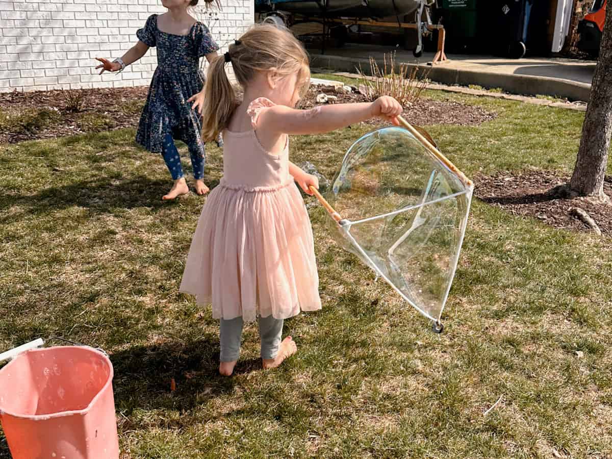 child making a giant bubble with DIY bubble wand and bubble solution.