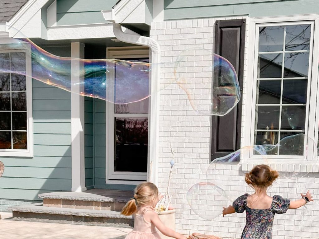 2 girls chasing after giant bubbles floating in the air