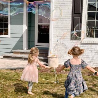 2 girls in spring dresses chasing after large bubbles