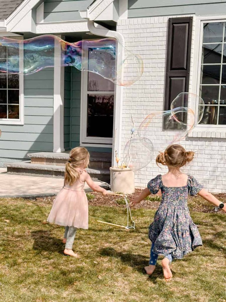 2 girls in spring dresses chasing after large bubbles