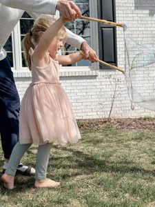 child in pink twirl dressed holding the giant bubble wand blowing large bubble