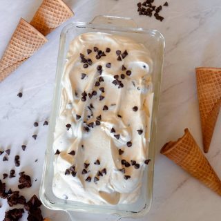 No churn ice ceram in bread pan with waffle cones and chocolate cookie dough on table around it