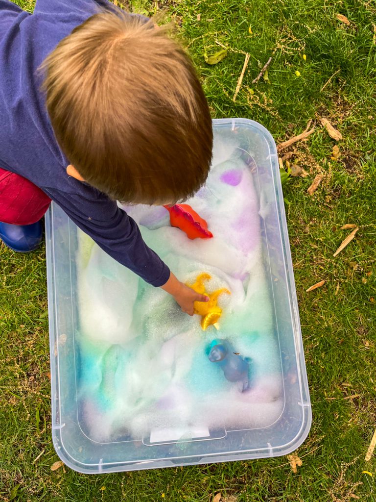 boy reaching down into bin of rainbow foam to get a dinosaur