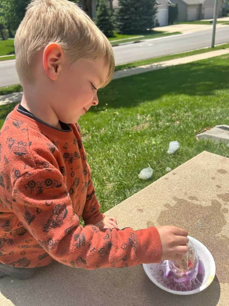 child dipping bubble bkower in bubble solution on the sidewalk