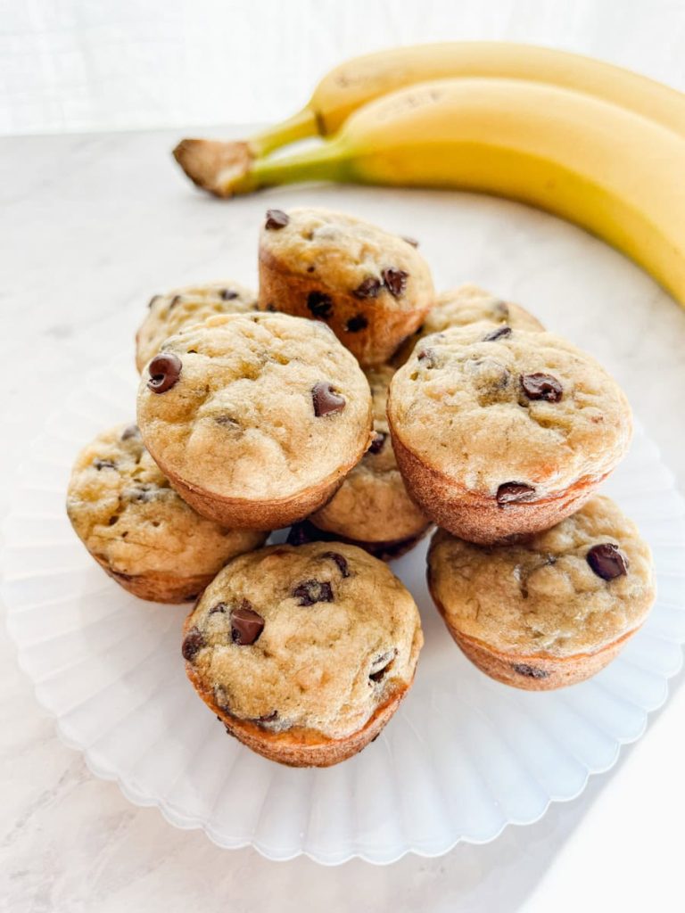 mini banana chocolate chip muffins stacked on a plate next to bananas