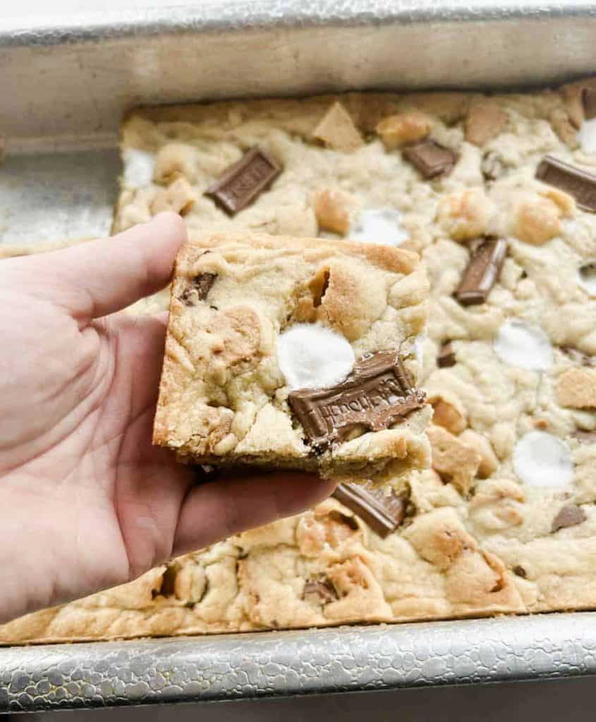 photo of person holding a smores bar with the pan of bars in the background