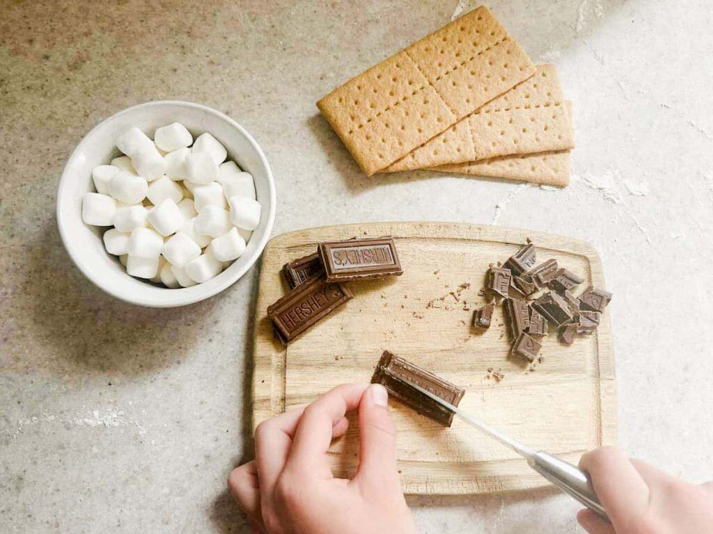 photo of hand cutting the chocolate bars with marshmallows and graham crackers next to the cutting board