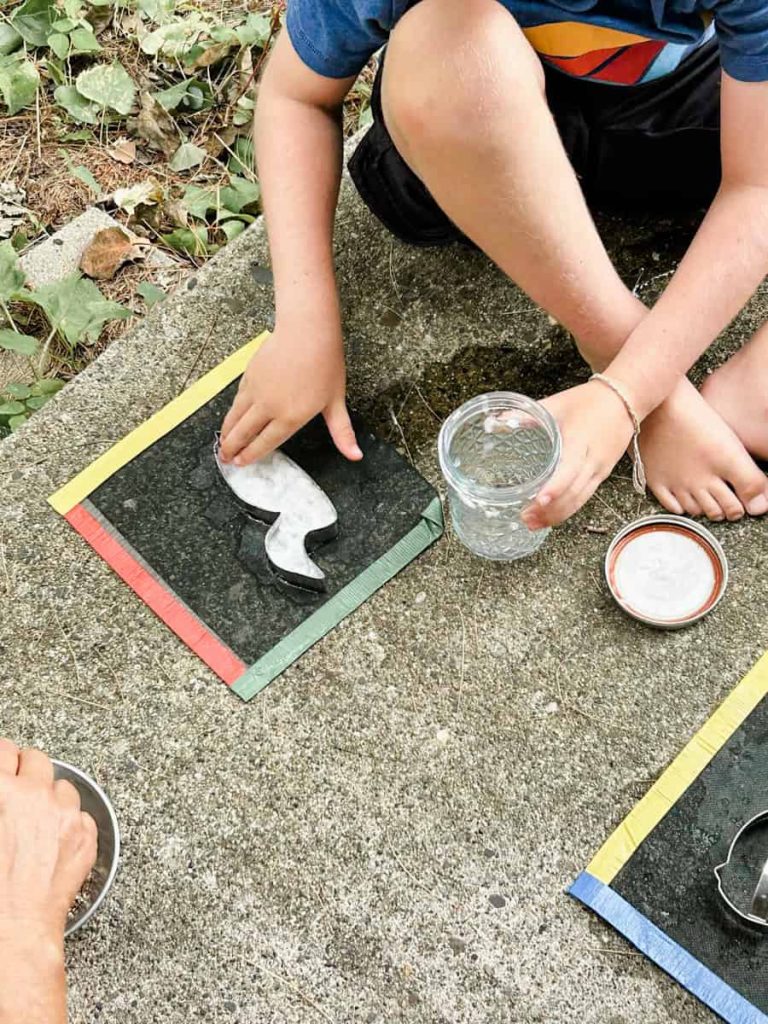 child pushing down the paper mixture into a cookie cutter shape with screen underneath
