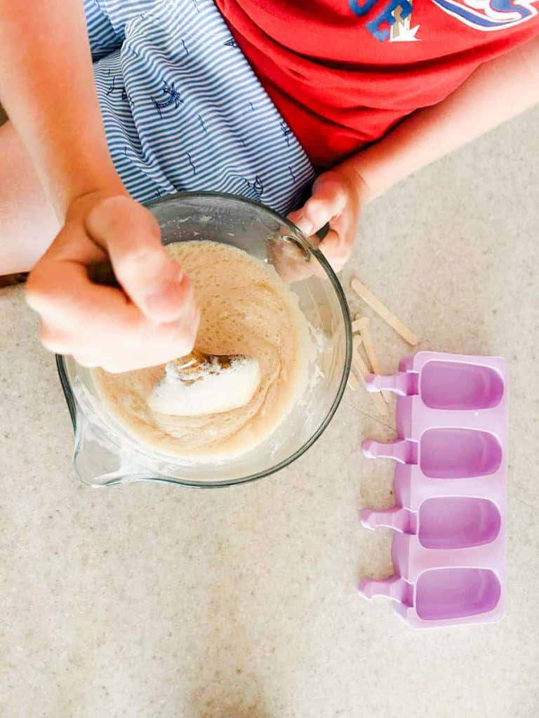 child mixing the ice cream and root beer mixture in a glass bowl
