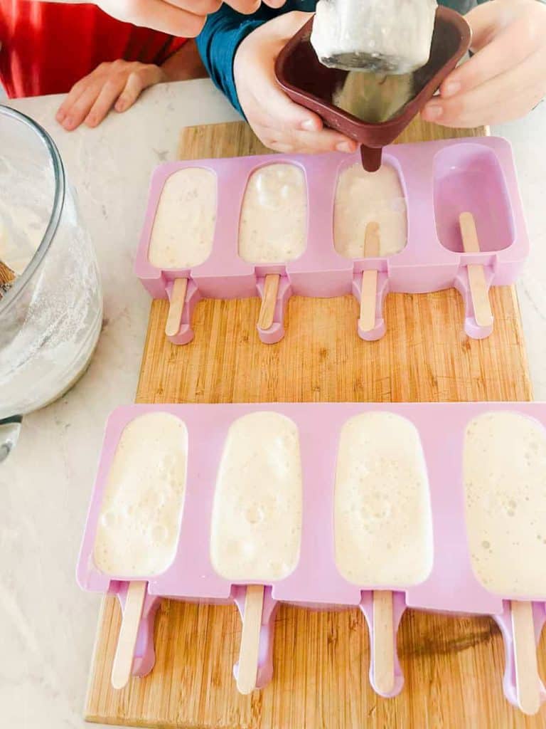 root beer popsicle mixture being poured into silicone popsicle mold with funnel