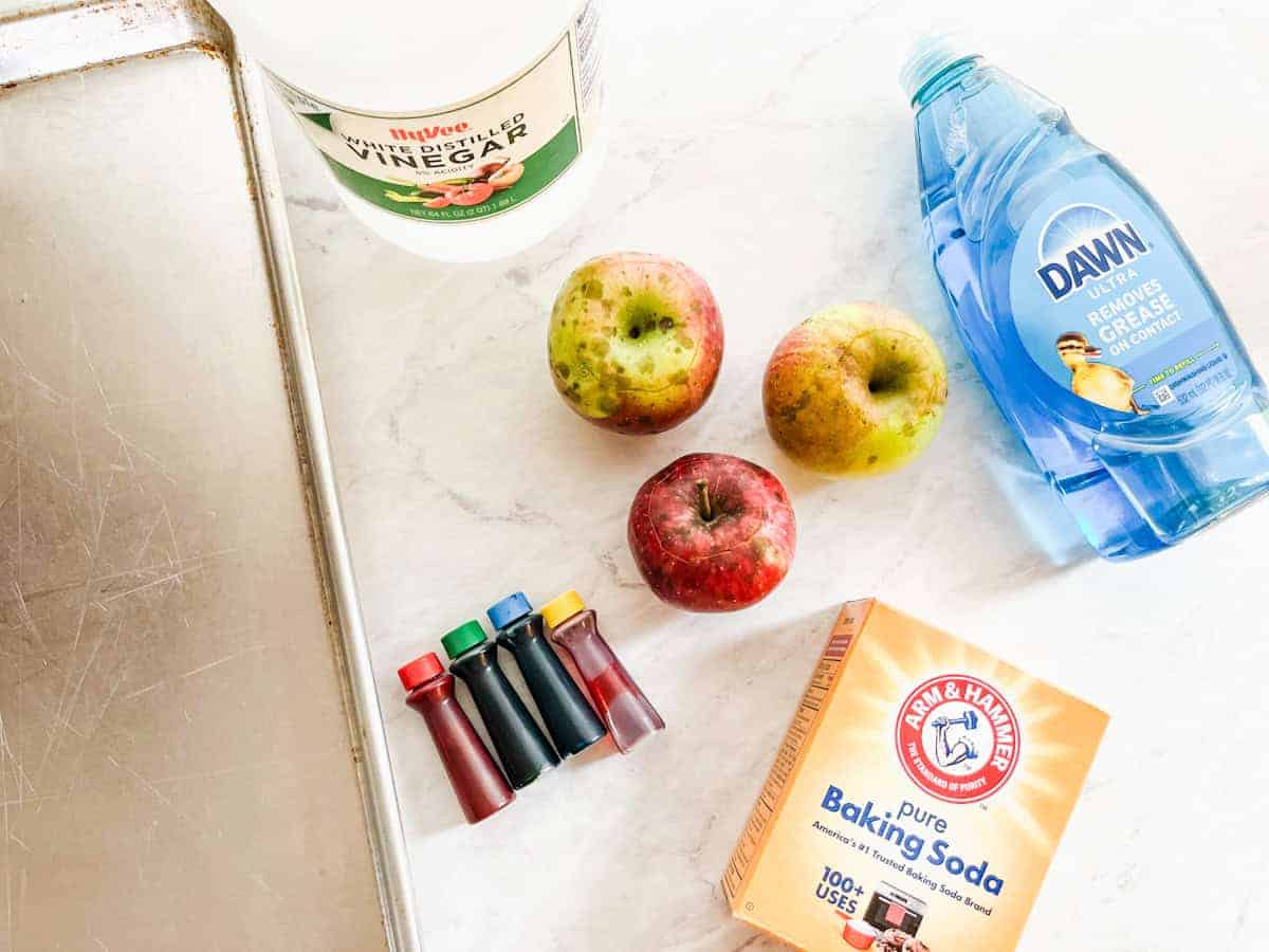 pan on counter with apples, food coloring, dish soap, baking soda and vinegar.