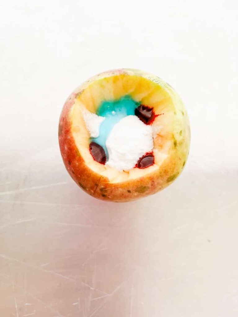 apple with baking soda, dish soap, and food coloring in center