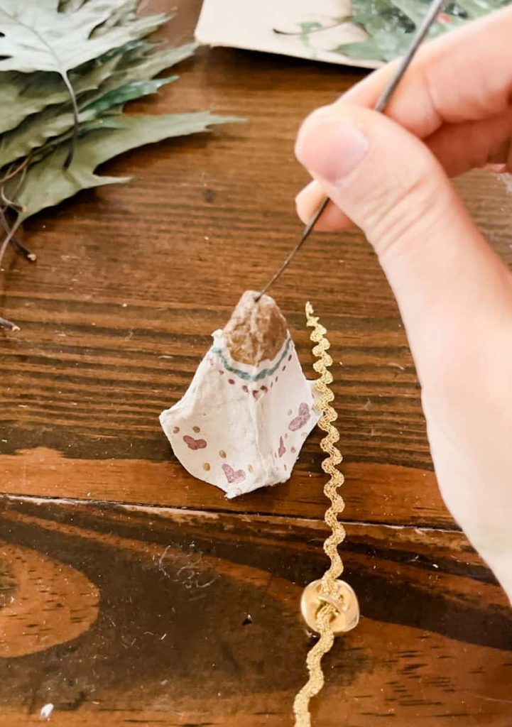 person stringing bell through egg carton jingle bell
