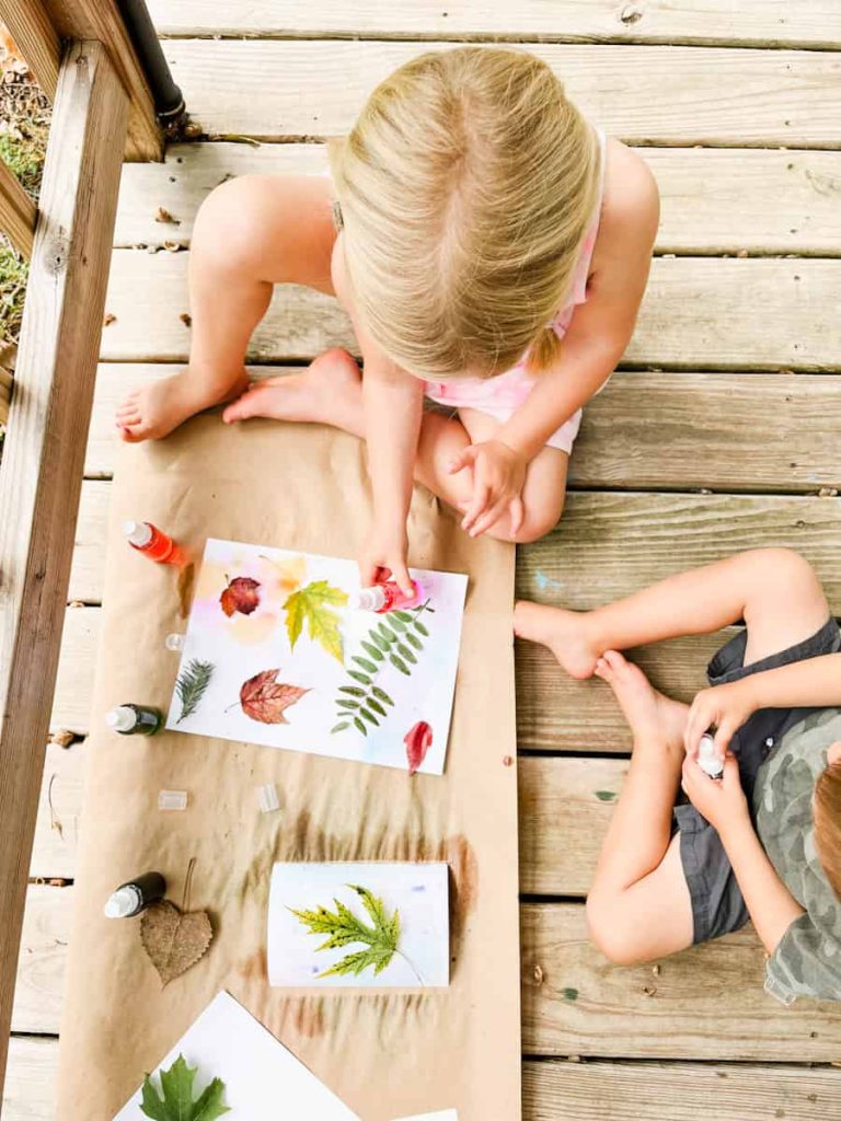two children sitting down spray painting leaves 