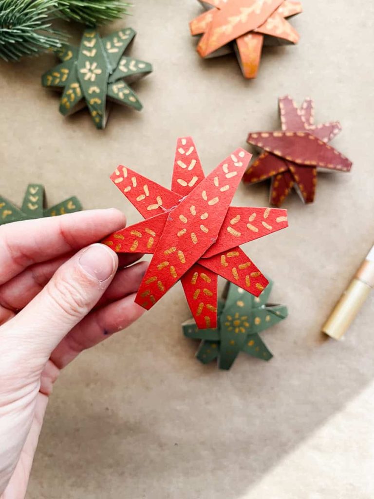 red christmas star made out of paper rolls held up in front of other finished Christmas stars