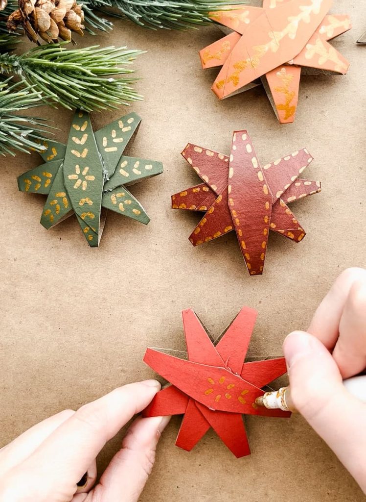person drawing a design on the finished 8 point christmas star next to other finished christmas stars on the table