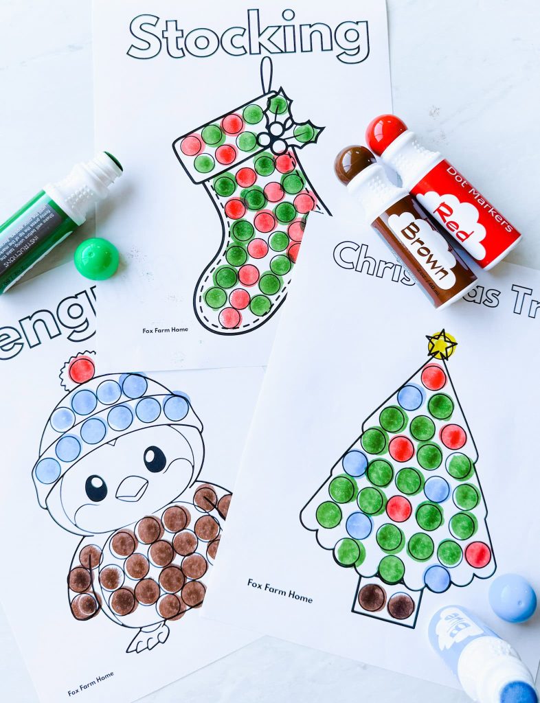 completed penguin, christmas tree and stocking dot marker printables with dot marker sitting on pages